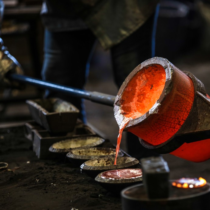 Schmelztiegel mit rot glühendem, flüssigen Metall beim Gießen (vergrößerte Bildansicht wird geöffnet)
