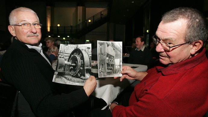 Zwei Männer halten historische Fotos in Händen