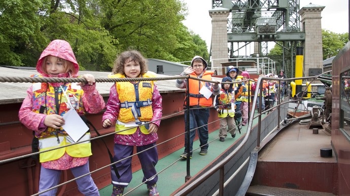 Kinder laufen über das Deck eines Schiffes, im Hintergrund das Schiffshebewerk