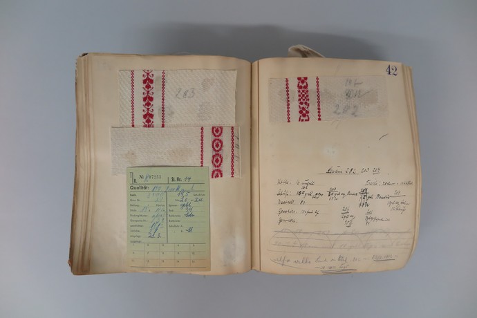 Ein offenes Produktionsbuch zeigt handschriftliche Notizen und Daten zu den Stoffen