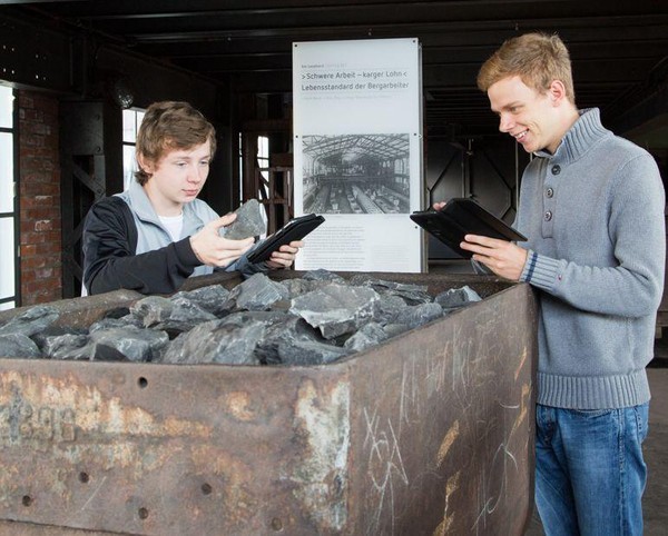 Zwei junge Männer mit Tabletts an einer Lore mit Kohle.